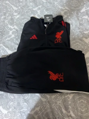Liverpool tränings kit  - Liverpool tränings kit svart röd och texten markerad med vit text. Storlek M men jag har S och den passa perfekt så passar både S och M. Väldigt skön att ha på sig och passar dig som gillar laget och går i fotboll o vill ha nögot varmt att ha på sig. PRIS KAN DISKUTERAS!
