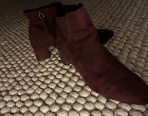 Vinröda mocka stövletter med klack - Säljer ett par snygga vinröda stövletter i mjuk mocka med rund tå och låg klack. Skorna har dragkedja på sidan för enkel på- och avtagning. Storlek 41, men passar som storlek 40.