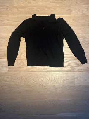 Svart stickad tröja med half zip från Uniqlo - Svart stickad tröja från Uniqlo i storlek M. Tröjan har en snygg krage och half zip framtill, vilket ger en cool och modern look. Långärmad och i mjukt material som passar perfekt när det är lite kyligare ute.