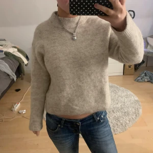 Beige stickad tröj - Mysig beige stickad tröja med långa ärmar. Tröjan har en rak, något boxig passform och är perfekt för lager på lager under kyliga dagar. Materialet känns mjukt och värmande, och färgen är lätt att matcha till allt.