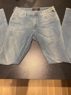 Replay ljusblå jeans 30/30 - Snygga ljusblå jeans från Replay. Klassisk femficksdesign med Replay-logga på fickan och bak vid midjan. Jeansen har en rak passform och är tillverkade i mjukt denimtyg med subtila slitningar för en cool look.