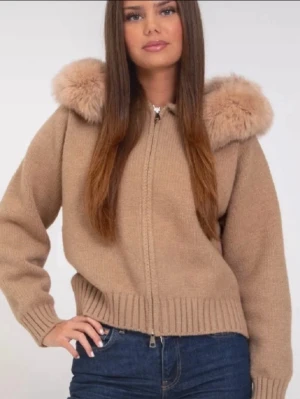 Beige cardigan jacka med pälsdetalj från Alessa - Säljer en beige cardigan jacka med fluffiga pälsdetaljer på axlarna och huva. Jackan är stickad i mjukt material och har dragkedja framtill samt ribbade muddar vid ärmslut och nederkant. Perfekt för dig som gillar chill och cozy vibes. OBS lappen är bortklippt