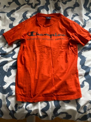 Orange Champion t-shirt X-Large - Snygg orange t-shirt från Champion i storlek X-Large. T-shirten har klassisk rund hals, korta ärmar och tryckt logga på bröstet. Tillverkad i mjuk bomull som är skön mot huden. Perfekt för dig som gillar sportiga och stilrena plagg.