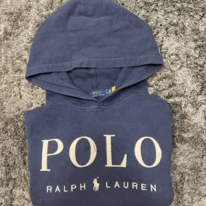 Mörkblå hoodie från Polo Ralph Lauren - Snygg mörkblå hoodie från Polo Ralph Lauren med stor broderad logga på bröstet. Tillverkad i mjuk bomull. Klassisk och stilren design som alltid funkarStår storlek M men passar perfekt på XS.  Lite slitning på O