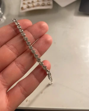 Glittrigt silverarmband med stenar - Snyggt armband i silverfärg med glittrande stenar längs hela bandet. Armbandet har en smal och elegant design med justerbar kedja och karbinlås. Perfekt för dig som gillar att addera lite extra bling till din stil.