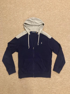 Blå och grå hoodie från Polo Ralph Lauren - Ralph Lauren hoodie storlek L i mycket bra skick, det finns inga synliga defekter och den är sparsamt använd. Hör av er om frågor!
