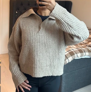 Beige stickad tröja med krage - Säljer en beige stickad tröja med bred krage och v-ringad öppning framtill. Tröjan har en loose passform och långa ärmar med ribbade muddar. Perfekt för dig som gillar chill och stilren look. Supermysig och enkel att matcha med jeans eller leggings.