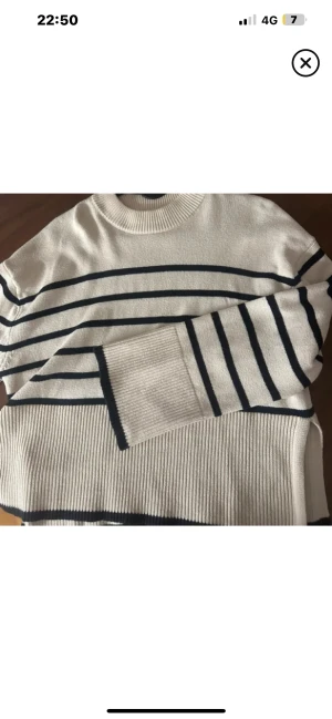 Randig beige stickad tröja - Snygg beige stickad tröja med svarta horisontella ränder. Tröjan har ribbad rund hals och muddar, samt långärmad passform. Perfekt för dig som gillar klassisk stil med en twist. Passar till jeans eller kjol för en chill look.