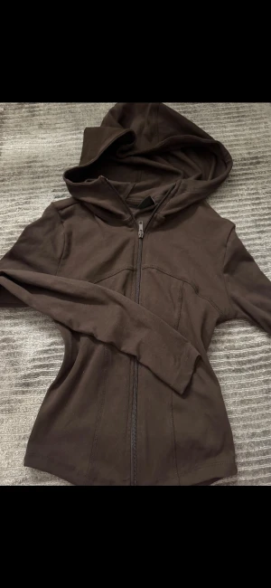 Brun hoodie med dragkedja Gina Tricot - Snygg brun hoodie från Gina Tricot i storlek XS. Tröjan har hel dragkedja framtill, huva och långa ärmar. Tillverkad i mjuk bomull som är skön mot huden. Perfekt för chill dagar och enkel att matcha med jeans eller leggings.