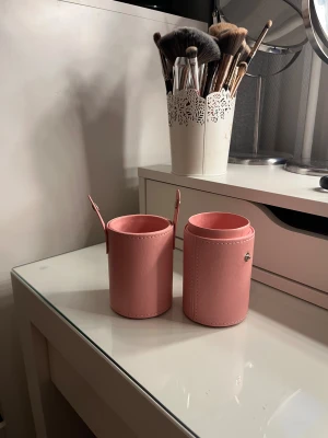 Rosa cylinderfodral för sminkborstar - Säljer ett snyggt cylinderformat fodral i ljusrosa konstläder, perfekt för att förvara och organisera dina sminkborstar. Fodralet har två delar som kan sättas ihop med tryckknappar på sidorna. Stilren design som gör det enkelt att ta med borstarna överallt.