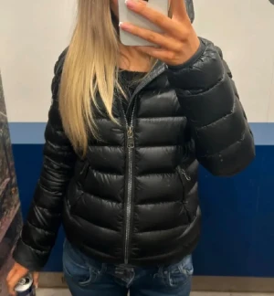 Svart pufferjacka från Colmar - Säljer en svart pufferjacka från Colmar med huva och dragkedja. klassisk logga på ärmen. Perfekt för kalla dagar och riktigt snygg till jeans eller mjukis.