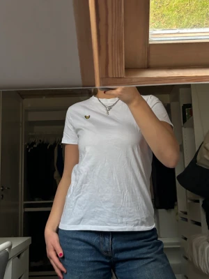 Vit t-shirt från Lyle & Scott - Vit t-shirt från Lyle & Scott Junior med klassisk passform och korta ärmar. T-shirten har en liten gul broderad fågel på bröstet och är gjord i mjuk bomull. Perfekt basic med snygg detalj som funkar till jeans eller shorts. Nästan aldrig använd🩷Står inte riktigt någon storlek men skulle säga typ XS!! 