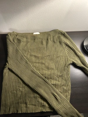 Olivgrön ribbad tröja från H&M - Säljer en olivgrön långärmad tröja från H&M i storlek S. Tröjan har ett ribbat mönster och är tillverkad i mjuk bomullsmix. Den har en klassisk rund hals och sitter snyggt med normal passform. Perfekt för dig som gillar stilrena och enkla plagg.