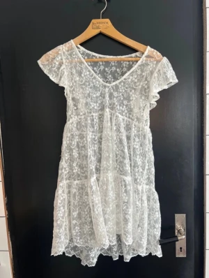 Vit spetsklänning med underklänning - Superfin vit kort spetsklänning med v-ringning och volangärmar. Medföljer en enkel vit underklänning med smala axelband. Perfekt för student med cykelbyxor under 😊