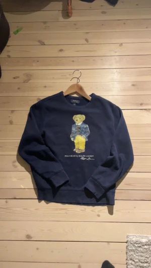 Mörkblå Polo Bear tröja Ralph Lauren - Säljer en mörkblå crewneck från Ralph Lauren med ikoniska Polo Bear-trycket framtill. Tröjan har rund halsringning och ribbade muddar vid ärmslut och nederkant. Perfekt statement piece för dig som gillar streetstyle och klassiska märken. Storlek L (14-16).                     Byten kan vara intressant 
