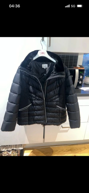 Svart pufferjacka från Isolde - Svart pufferjacka från Isolde med snygga detaljer som dragkedja och kontrastband vid fickorna. Jackan har en fluffig krage och quiltad design som ger en cool look. Perfekt för dig som gillar stil och värme under höst och vinter.