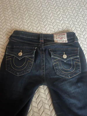 True Religion mörkblå jeans med kontrastsömmar - Säljer mina true religion byxor då de ej kommer till användning, de är mid waist men de är uppsydda så de är low waist, de är även uppsydda i affär. De har ett litet slitage längst ner på byxan, men inget märkvärdigt