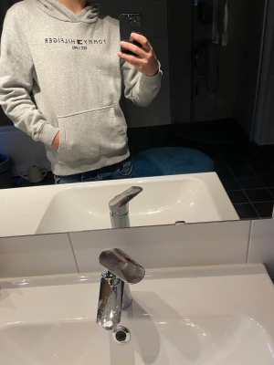 Grå hoodie från Tommy Hilfiger - Bara att höra av sig om du undrar något!☺️Säljer en stilren grå hoodie från Tommy Hilfiger med broderad logga och text på bröstet. Tröjan har huva, magficka och ribbade muddar. Perfekt för dig som gillar klassisk streetstyle och vill ha något bekvämt och snyggt.