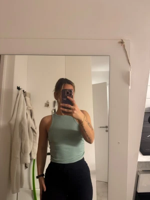 Ljusgrön ribbad linnetopp - Säljer en ljusgrön croppad linnetopp med ribbad struktur och rundad hals. Toppen är ärmlös och har en slim passform som sitter snyggt mot kroppen. Perfekt för dig som gillar stilrena och enkla plagg med fräsch färg.