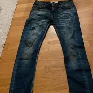 Saligiaas7 med slitningar - Säljer ett par coola blå jeans från Saligiaas7 i storlek M. Jeansen har snygga slitningar och patchdetaljer på framsidan, samt klassisk femficksdesign. Materialet är jeans och passformen är rak med normal midja. Perfekt för dig som gillar en edgy streetstil.