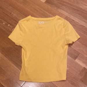 Gul ribbad topp XXS - Säljer en enkel och fräsch gul ribbad topp i storlek XXS. Toppen har korta ärmar, rund halsringning och är gjord i ett mjukt, stretchigt material som sitter snyggt på kroppen. Perfekt till jeans eller kjol för en färgglad look.