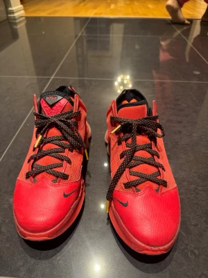 Röda Nike Lebron 19 Low  sneakers - Säljer ett par röda Nike LeBron sneakers med svart och rödprickiga snören och gulddetaljer. Skorna har en robust platt sula med Nike React-teknologi, mesh och skinn på ovandelen samt LeBron-logga på tungan. Perfekt för dig som gillar basketstil och vill sticka ut.