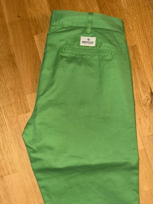 Gröna chinos från Morris - Snygga gröna chinos från Morris med raka ben och klassisk passform. Byxorna har bälteshällor, knappgylf och två bakfickor med knappdetalj. Tillverkade i mjuk bomull som känns skön mot huden. Perfekta för dig som vill sticka ut med färg.