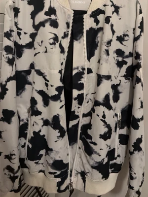 Svartvit bomberjacka från Galagowear st.S-M - Säljer en bomberjacka från Galagowear i svartvitt mönster med broderad logga och siffran 07 på ryggen. Jackan har dragkedja framtill, ribbade muddar och två fickor med dragkedja. Perfekt statement-plagg för dig som gillar streetwear.