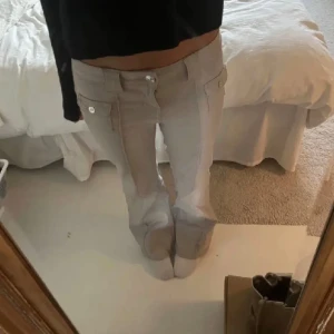 H&M byxor  - Säljer ett par ljusbeige byxor med stora fickor och knappar framtill. Byxorna har låg midja och raka utsvängda ben med en snygg söm längs framsidan. Perfekta till en enkel topp eller hoodie.