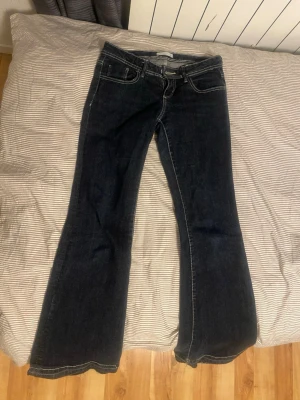 Mörkblå bootcut jeans från Perfect Jeans - Mörkblå jeans med bootcut från Perfect Jeans i storlek 36. Klassisk femficksmodell med kontrastsömmar och råa, fransiga benslut för en avslappnad vibe. Tillverkade i slitstarkt denimtyg som ger en snygg passform.