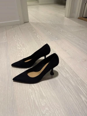 Svarta pumps - Säljer ett par svarta pumps från H&M med snygg spetsig tå och låg klack. Skorna är gjorda i mocka och har en klassisk siluett som ger en stilren vibe. Använts 2 gånger