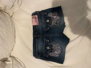Mörkblå jeansshorts WeTweens - Säljer ett par mörkblå jeansshorts från WeTweens by KappAhl. Shortsen har råa, fransiga kanter och snygga broderade fjärilar i rosa och silver på bakfickorna. Märkeslapp i rosa med glitterdetaljer och klassisk femficksmodell. Perfekta för sommaren! 