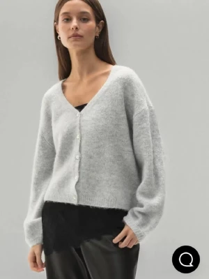 Ljusgrå kofta med knappar - Mysig ljusgrå kofta med v-ringning och pärlemorknappar. Koftan har en loose passform och är stickad i ett mjukt material. Perfekt att slänga på sig över ett linne eller t-shirt.