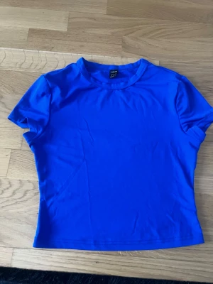 Blå tight t-shirt från SHEIN - En enkel och stilren blå t-shirt från SHEIN i storlek S. Modellen är tight med korta ärmar och rund halsringning. Perfekt att matcha med jeans eller kjol för en clean look.