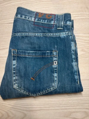 Dondup jeans strlk 34 - Säljer ett par klassiska blå jeansbyxor från dondup med raka ben och snygga slitningar. Jeansen har fem fickor, kontrastsömmar och en cool detalj på bakfickan. Perfekta till vardags och passar till det mesta. Materialet är tåligt jeans i bomull.