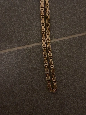 Guldfärgad kedja  - Säljer en chunky guldfärgad kedja med boxlänkar. Kedjan har en cool, robust design och passar perfekt som accessoar för att lyfta din outfit. Länkarna är fyrkantiga och ger ett stilrent men ändå edgy intryck. !Guld platterad!