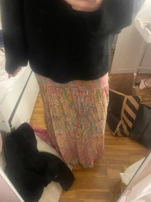 Färgglad långkjol med paisleymönster - Säljer en långkjol med färgstarkt paisleymönster i orange, rosa, blått och grönt. Kjolen har en flowy passform och är gjord i ett tunt, mjukt tyg som känns luftigt.