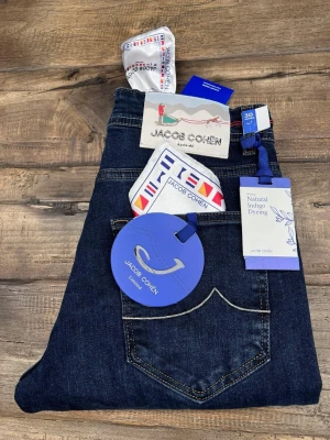Jacob Cohën mörkblå jeans med brodyr - Snygga mörkblå jeans från Jacob Cohën med cool broderad detalj vid fickan och kontrastsömmar. Jeansen har klassisk femficksdesign, naturlig indigofärgning och exklusiva etiketter. Perfekta för dig som gillar premiumkänsla och stilren look.