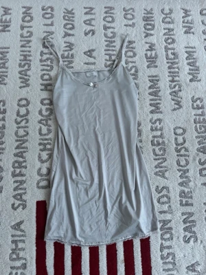 Beige natt klänning med spets från Cream - Supersöt beige natt klänning från Cream med tunna axelband och dekorativ spets längs både halsringning och nederkant. Klänningen har en liten rosett framtill och är gjord i mjukt, lent material som känns skönt mot huden. .