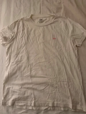 Vit t-shirt - Lee  - Säljer en enkel vit t-shirt från Lee i storlek S. T-shirten har korta ärmar, rund hals och en liten röd Lee-logga på bröstet. Materialet är mjuk bomull och passformen är normal. Perfekt till jeans eller shorts. Säljer pga får ingen användning’