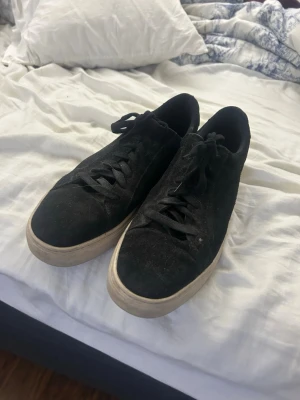 Svarta mockasneakers med vit sula - Säljer ett par svarta sneakers i mocka med klassisk rund tå och snörning. Skorna har en vit, platt sula som ger en clean kontrast till det svarta ovandelen. Perfekta till jeans eller shorts för en chill och stilren look.