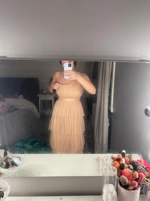 Ljusrosa långklänning oneshoulder - Säljer en ljusrosa långklänning med flera lager volang i tyll. Klänningen har oneshoulder-design och markerad midja, vilket ger en elegant och flowy look. Perfekt för bal. Klänningen är använd en gång och har inga täcken på användning, klänningen är lite lång för mig och jag är 164 cm lång. Klänningen är ljusare rosa i värkligheten än på bilderna!