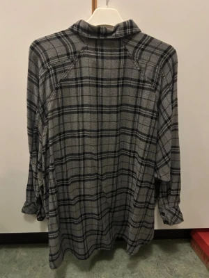 Grå rutig skjorta Urban Outfitters - Säljer en grå och svart rutig skjorta från Urban Outfitters. Skjortan har klassisk krage, knappstängning framtill och en bröstficka. Materialet är mjukt och känns som bomull, perfekt för chill dagar. Långärmad och loose fit för avslappnad stil.