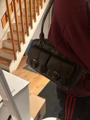 Brun vintage axelväska - Brun vintage axelväska med två framfickor med spännen i guld och dubbla axelremmar. Väskan har dragkedja upptill och en liten innerficka. Toppen skick.💞