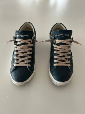 Philippe Model  sneakers i skinn - Snygga svarta sneakers från Philippe Model med beige snörning och vit sula. Skorna är tillverkade i skinn och har en klassisk låg profil med rund tå. Perfekta för dig som gillar stilrena och tidlösa sneakers med premiumkänsla.