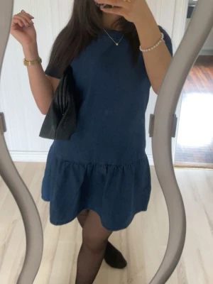 Mörkblå kort klänning i bomull - Säljer en enkel och stilren mörkblå kort klänning med rund hals och lös passform. Klänningen har en lätt volang nedtill och är sydd i mjuk bomull, perfekt för en avslappnad look. Ärmarna är korta och modellen är riktigt bekväm.