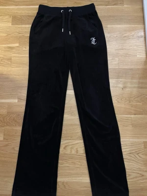 Svarta Juicy Couture mjukisbyxor XS - Svarta mjukisbyxor från Juicy Couture i storlek XS. Byxorna har snörning i midjan och är gjorda i mjuk sammet. På framsidan finns en glittrig JC-logga och på baksidan står det ”Juicy”. Perfekt för chill dagar.
