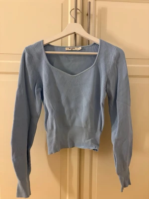 Ljusblå ribbad tröja från NA-KD - Supersnygg ljusblå ribbad tröja från NA-KD med lång ärm och bred, fyrkantig ringning. Tröjan är croppad och har en figurnära passform som framhäver midjan. Perfekt till jeans eller kjol för en fräsch look.