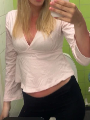 Gina Tricot tie top - Säljer en ljusrosa omlottopp med v-ringning och långa ärmar. Toppen har en feminin passform och är tillverkad i ett mjukt bomullsliknande material. Perfekt att styla med jeans eller kjol för en fräsch look.