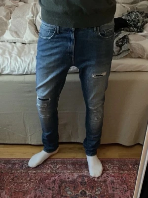 Tiger Of Sweden Jeans - Säljer ett par snygga blå jeans från T/J med coola slitningar på framsidan. Skick || 9/10, storlek 32/34. Perfekta för en avslappnad stil. Slim fit.